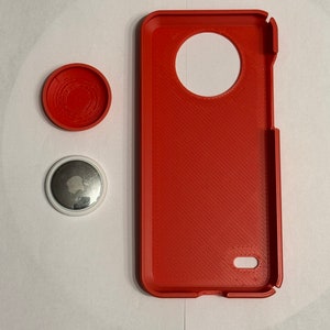May include: A red phone case with a large circular cutout on the back. The case is made of a textured material. There are two small round objects next to the case. One is red and the other is white with a silver apple logo.