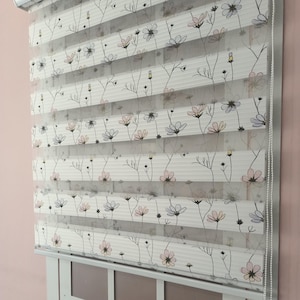 Può includere: Tende a rullo bianche per finestre con un motivo floreale con fiori rosa, gialli e blu. Le tende sono realizzate in tessuto trasparente e hanno un cordoncino bianco.