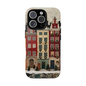 Puede incluir: Una funda para smartphone con una ilustración impresa de tres edificios estrechos de varias plantas en un entorno invernal nevado. Los edificios son rojos, beige y rojos, decorados con coronas verdes en las ventanas y pequeños abetos en la base.