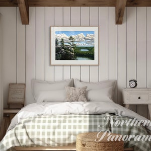 May include: A framed landscape painting of a lake and forest scene with a blue sky and white clouds. The painting is hanging on a white wood paneled wall in a bedroom with a bed, nightstand, and lamp.