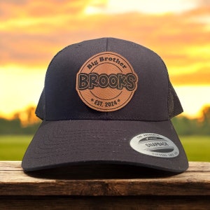 Puede incluir: Gorra de camionero negra de malla con un parche de cuero marrón que dice "Big Brother Brooks *EST. 2024*" en letras negras.