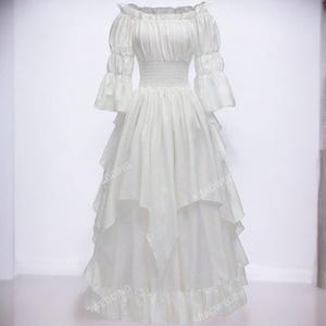 K&ouml;nnte beinhalten: Ein wei&szlig;es, schulterfreies Kleid mit einem Stufenrock und Puff&auml;rmeln. Das Kleid hat ein tailliertes Oberteil und einen flie&szlig;enden Rock.