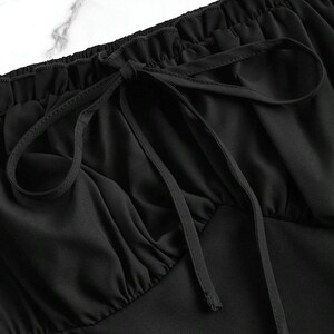 May include: Close-up of a black top with a gathered neckline and a drawstring tie. The fabric is smooth and drapes softly, with subtle folds adding texture. The drawstring is tied in a bow, creating a delicate detail.