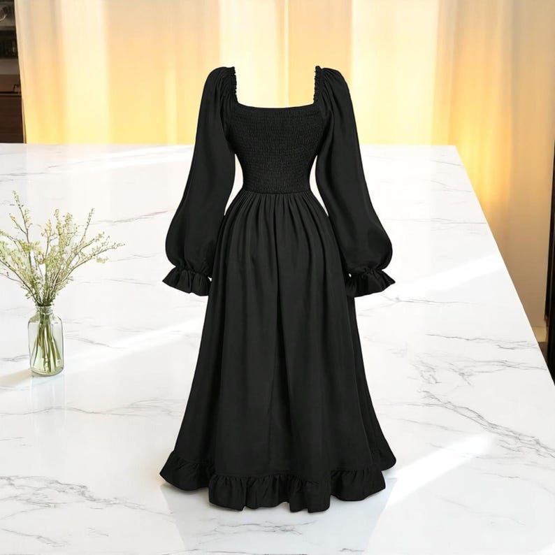 May include: A black midi dress with a square neckline and long, puffed sleeves. The dress features a fitted bodice and a flowing skirt with a ruffled hem. The dress is displayed on a white marble surface.