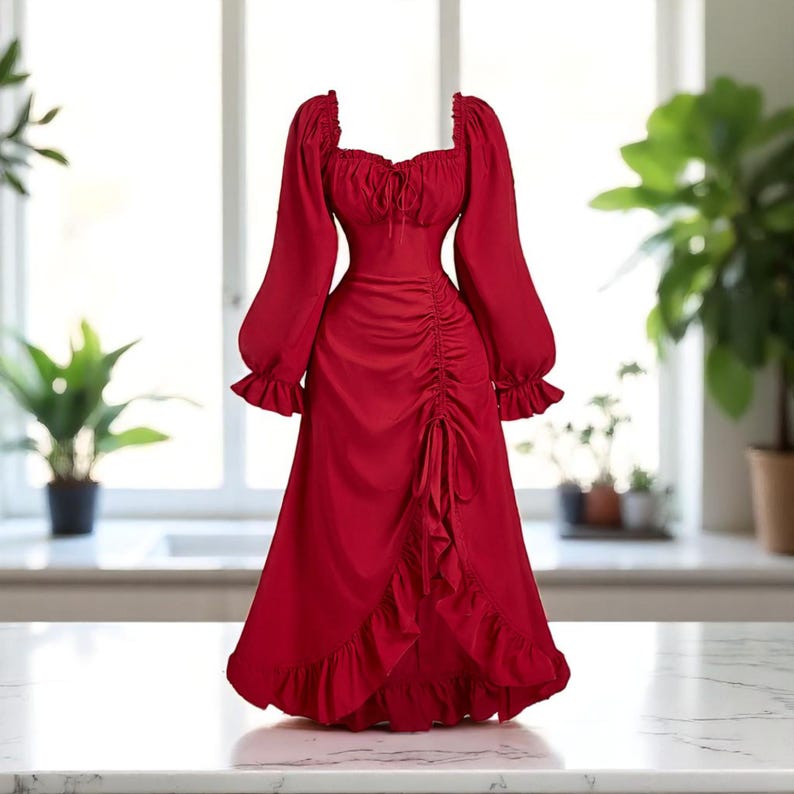 May include: A vibrant red dress with long, puffed sleeves and a square neckline. The dress features a ruched bodice and a flowing skirt with a ruffled hem. The dress is made of a smooth, possibly satin-like fabric, and is displayed on a white surface.