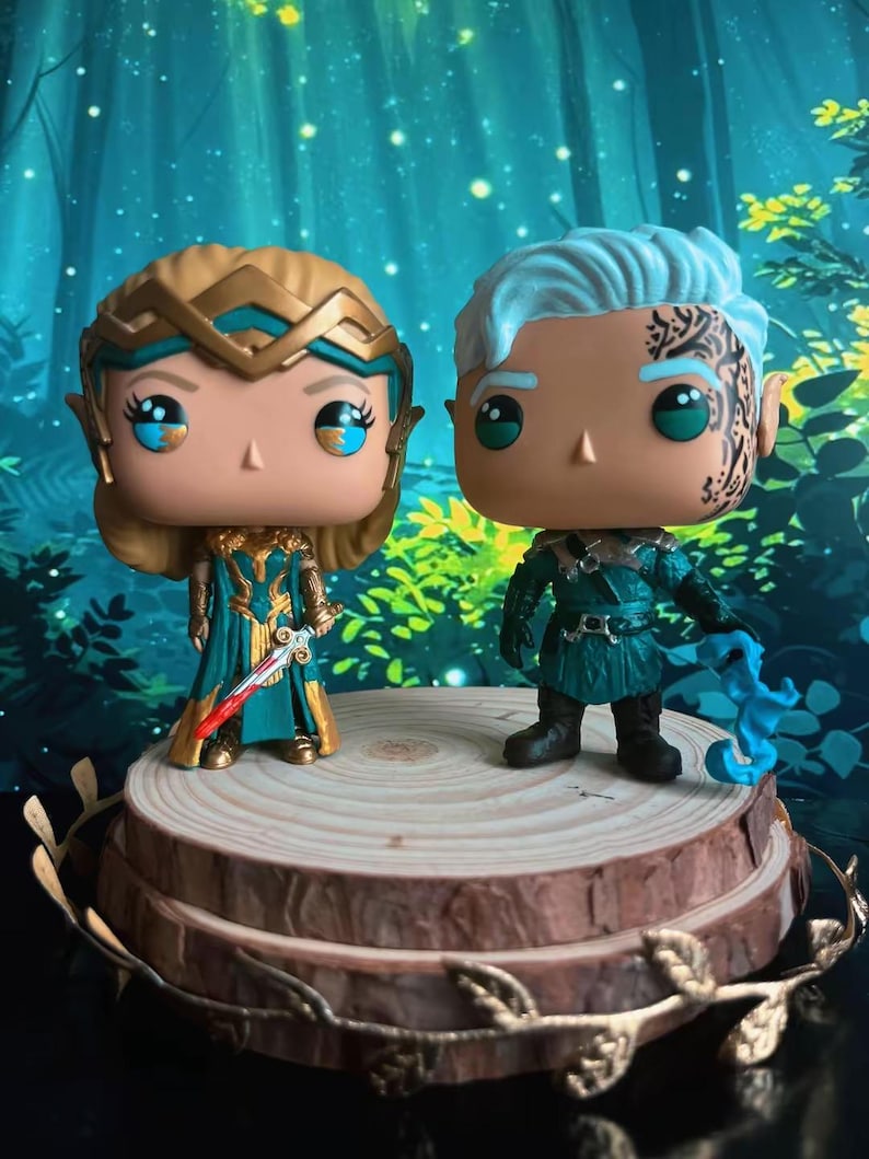 May include: Two Funko Pop figures of fantasy characters. One figure has blonde hair and a teal and gold outfit, holding a sword. The other figure has blue hair and a teal outfit, holding a blue object. They are displayed on a wooden platform.