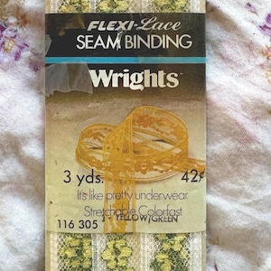 Könnte beinhalten: Eine Packung Flexi-Lace Seam Binding von Wrights. Die cremefarbene Spitze hat gelbe und grüne Blumenmuster. Auf der Verpackung steht "3 yds." und "It's like pretty underwear."