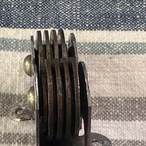 Puede incluir: Primer plano de un objeto met&aacute;lico vintage con m&uacute;ltiples cuchillas circulares. Las cuchillas est&aacute;n apiladas y sujetas con remaches. El objeto tiene un marco morado y un soporte de montaje plateado. Las cuchillas parecen oxidadas.
