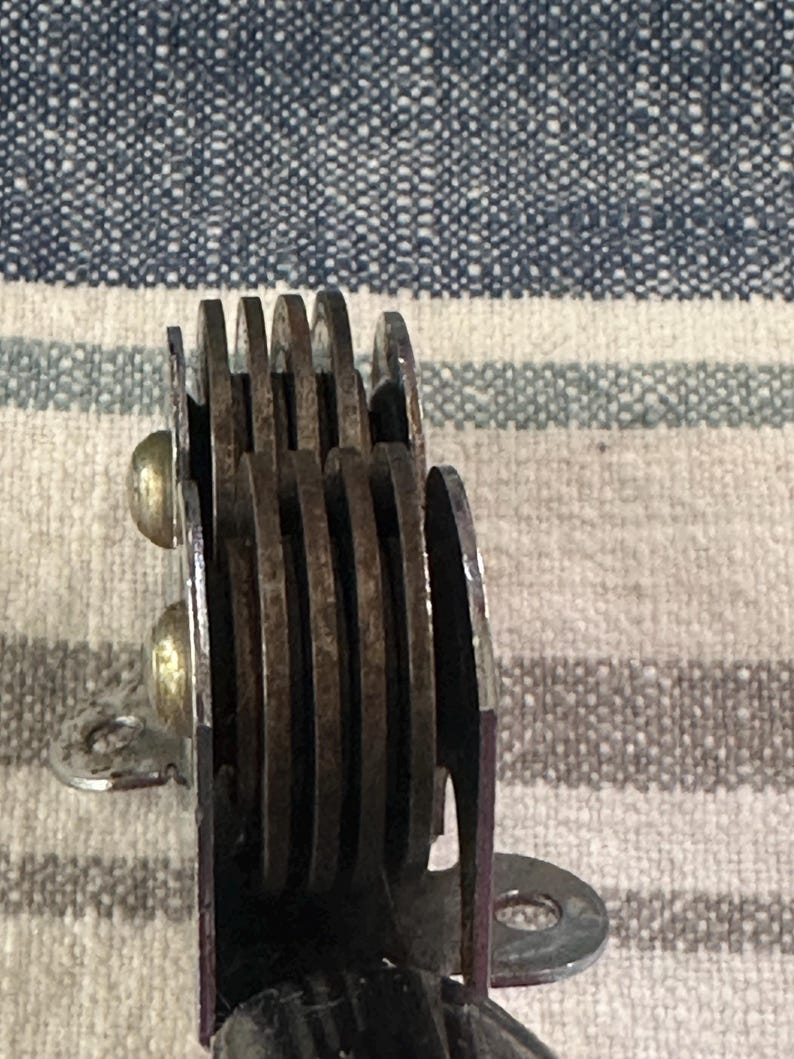 Puede incluir: Primer plano de un objeto met&aacute;lico vintage con m&uacute;ltiples cuchillas circulares. Las cuchillas est&aacute;n apiladas y sujetas con remaches. El objeto tiene un marco morado y un soporte de montaje plateado. Las cuchillas parecen oxidadas.