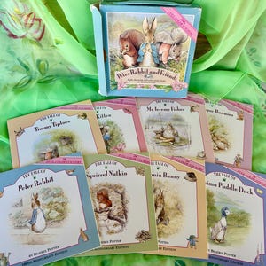 May include: A collection of children's books and a box set featuring illustrations of Peter Rabbit and friends. The books have colorful covers with titles like "Timmy Tiptoes" and "Squirrel Nutkin". The box set is light blue.