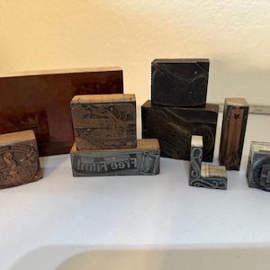 May include: A collection of vintage wooden printing blocks with various designs and text, including "Free Film" and "The American Souvenir Co."