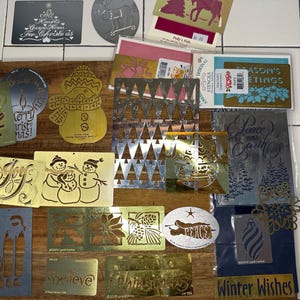 Könnte beinhalten: Eine Sammlung von Weihnachtsschablonen und dekorativen Metallausstanzungen. Designs umfassen Schneemänner, Weihnachtsbäume, Ornamente und die Wörter "Joy", "Peace on Earth" und "Winter Wishes". Die Schablonen sind in verschiedenen Farben, darunter Gold, Silber und Grün.