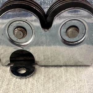 Puede incluir: Primer plano de un afilador de cuchillos manual. El afilador tiene un cuerpo de metal plateado con dos muelas y un mango negro. Las muelas est&aacute;n hechas de un material oscuro y est&aacute;n dise&ntilde;adas para afilar cuchillos.