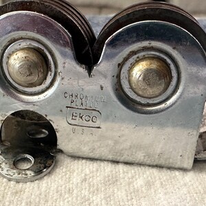 Puede incluir: Primer plano de un afilador de cuchillos cromado vintage. El afilador tiene dos ruedas giratorias y un mango. El texto "CHROMIUM PLATED" y "Ekco U.S.A." son visibles en el cuerpo met&aacute;lico.