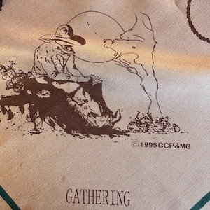 Op de afbeelding: Een beige en groene sjaal met een bruine illustratie van een cowboy op een paard, met de tekst "GATHERING 2000" en het copyright "©1995 CCP&MG". De sjaal heeft een groene rand.
