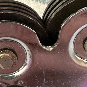 Puede incluir: Primer plano de un afilador de cuchillos vintage. El dispositivo presenta m&uacute;ltiples ruedas de afilado met&aacute;licas circulares y un cuerpo met&aacute;lico pulido. Las ruedas est&aacute;n apiladas y ligeramente desgastadas, lo que indica su uso. El afilador est&aacute; dise&ntilde;ado para restaurar el filo de los cuchillos.