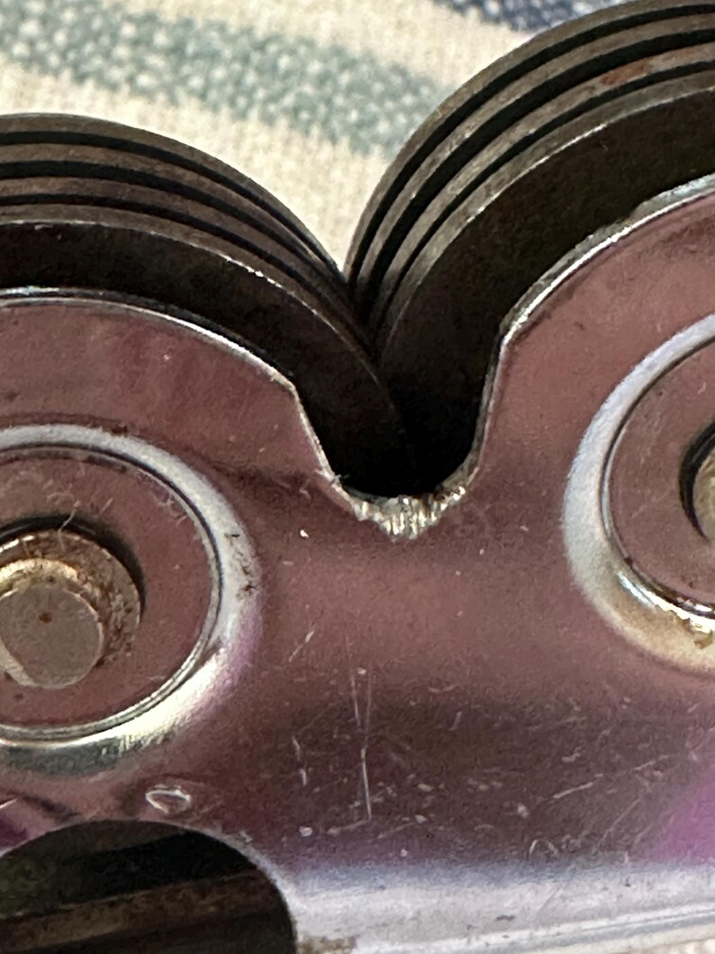 Puede incluir: Primer plano de un afilador de cuchillos vintage. El dispositivo presenta m&uacute;ltiples ruedas de afilado met&aacute;licas circulares y un cuerpo met&aacute;lico pulido. Las ruedas est&aacute;n apiladas y ligeramente desgastadas, lo que indica su uso. El afilador est&aacute; dise&ntilde;ado para restaurar el filo de los cuchillos.