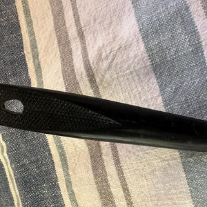 Puede incluir: Mango negro de utensilio de cocina con agarre texturizado y orificio para colgar. El mango est&aacute; unido a un utensilio de metal con m&uacute;ltiples p&uacute;as. El utensilio probablemente se utiliza para cocinar o servir alimentos.