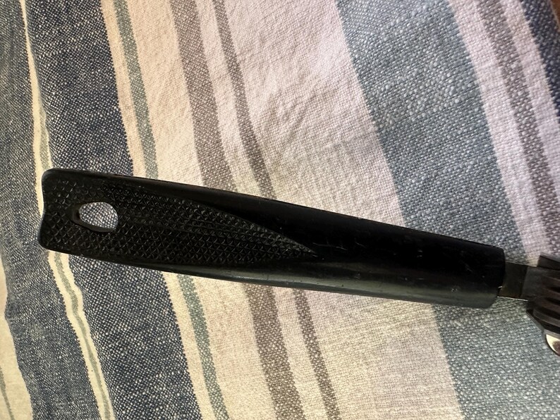 Puede incluir: Mango negro de utensilio de cocina con agarre texturizado y orificio para colgar. El mango est&aacute; unido a un utensilio de metal con m&uacute;ltiples p&uacute;as. El utensilio probablemente se utiliza para cocinar o servir alimentos.