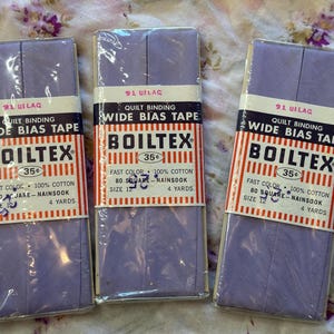 May include: Three packages of lavender Boiltex wide bias tape for quilt binding. Each package contains 4 yards of 100% cotton fabric, size 12, labeled as fast color and 80 square nainsook. The packaging features white, orange, and black text.