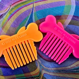 May include: Two plastic combs shaped like bones, one orange and one pink, with comb teeth. The combs have a fish-like design and the text "1992 M.I.I. CHINA" printed on them. The orange comb has the number "1" and the pink comb has the number "5".