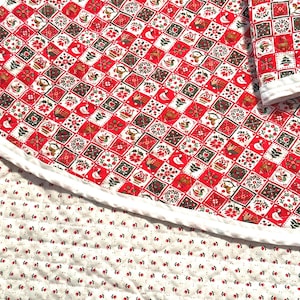 May include: A quilted fabric piece featuring a red and white grid pattern with small illustrations of geese, trees, and floral motifs, bordered by a white trim. The underside is a white fabric with a repeating pattern of tiny red flower buds.