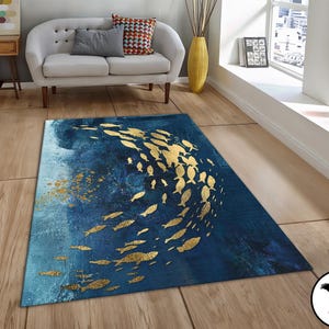 Puede incluir: Una alfombra azul y dorada con un dise&ntilde;o de peces nadando en un patr&oacute;n circular. La alfombra tiene un aspecto desgastado y texturizado.