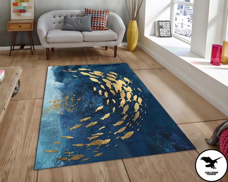 Puede incluir: Una alfombra azul y dorada con un dise&ntilde;o de peces nadando en un patr&oacute;n circular. La alfombra tiene un aspecto desgastado y texturizado.