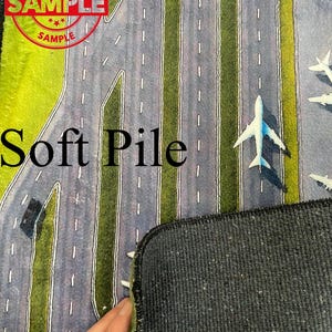 Puede incluir: Una alfombra de pelo suave con un dise&ntilde;o impreso de una pista de aeropuerto con aviones. La alfombra tiene un respaldo negro.
