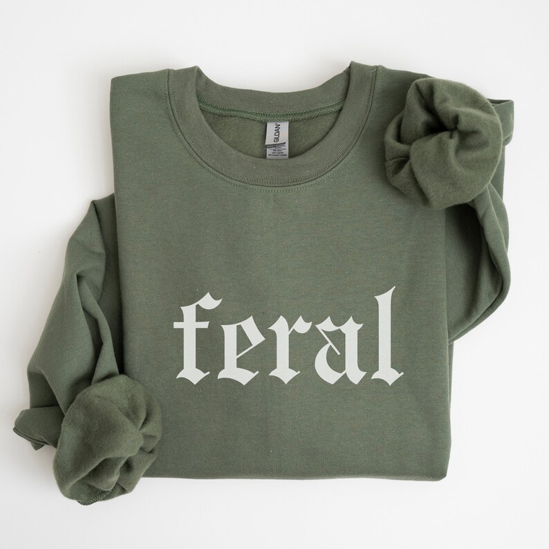 May include: A green sweatshirt with the word "feral" printed in white in a gothic font.