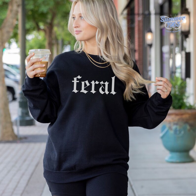 May include: Black sweatshirt with the word "feral" printed in white in a gothic font.