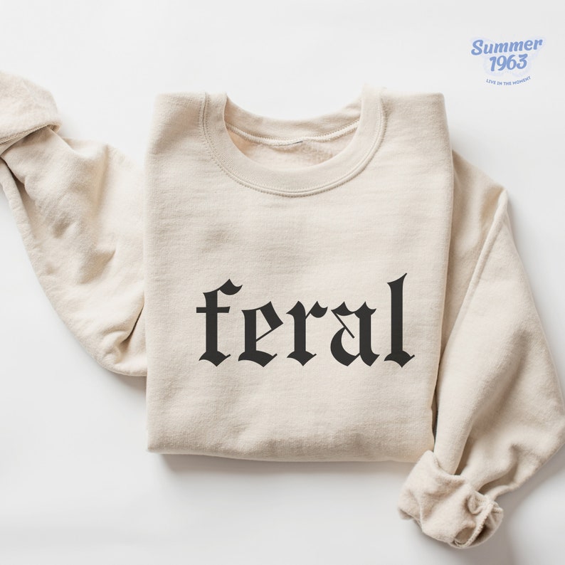 May include: A beige sweatshirt with the word "feral" printed in black gothic lettering.
