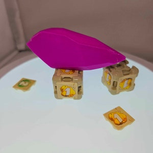 May include: A purple plastic piece balanced on top of two beige cube-shaped dice with a number "1" on each side. There are three additional beige squares with the number "1" on them.