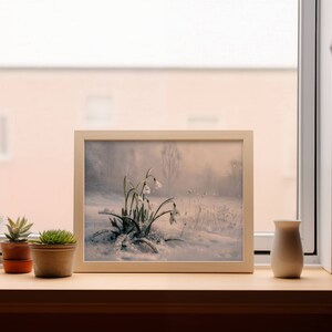 May include: A framed painting of a snowy landscape with white flowers in the foreground. The painting is on a windowsill with two potted succulents.
