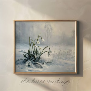 May include: A framed painting of a snowy forest scene with a cluster of white snowdrop flowers in the foreground. The flowers are in focus, while the background is blurred and hazy.