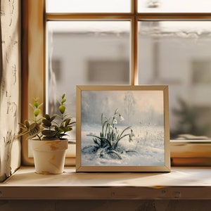 May include: A framed painting of white snowdrops blooming in a snowy landscape. The painting is in a white frame and is sitting on a wooden shelf.