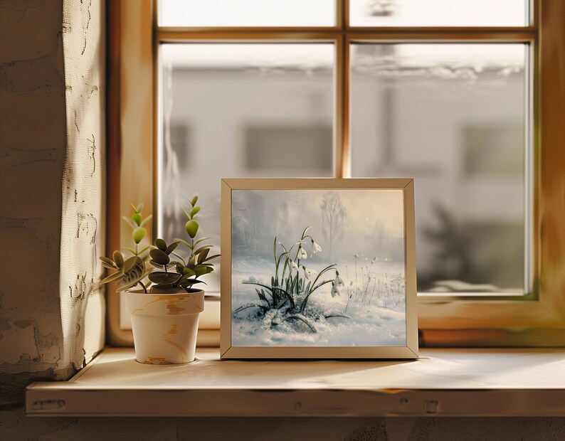 May include: A framed painting of white snowdrops blooming in a snowy landscape. The painting is in a white frame and is sitting on a wooden shelf.