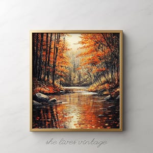 May include: A framed landscape painting depicting an autumn scene. The artwork features a river flowing through a forest with trees displaying vibrant orange and red foliage. The painting is in a gold frame, and the text "she lives vintage" is at the bottom.