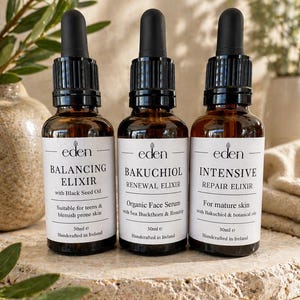 Könnte beinhalten: Drei braune Glasflaschen mit schwarzen Tropfern, beschriftet mit "BALANCING ELIXIR", "BAKUCHIOL RENEWAL ELIXIR" und "INTENSIVE REPAIR ELIXIR". Jede Flasche hat ein weißes Etikett mit schwarzem Text, einschließlich "eden" und Produktdetails. Die Flaschen sind je 30 ml groß und handgefertigt in Irland.