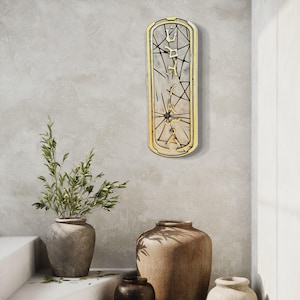 May include: A rectangular wall art piece with a gold-colored frame and a light-colored interior. The interior features a geometric design with black lines and text. The art is mounted on a light gray wall, with decorative vases and a plant in the foreground.
