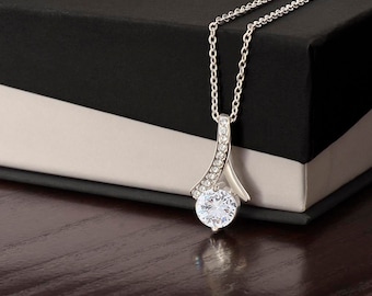May include: A silver necklace with a large, clear, round gemstone pendant. The pendant is set in a silver setting with smaller clear gemstones around the edge. The necklace is on a black and white box.