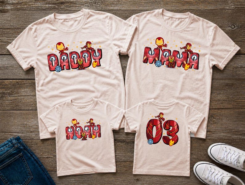 May include: Four light pink t-shirts with matching designs. Two shirts say "DADDY" and "MAMA" in red and black block letters with Iron Man graphics. The other two shirts say "NOAH" and "03" with similar graphics.