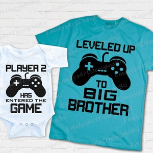 May include: Two white shirts with black text and a black video game controller graphic. The smaller shirt says "Player 2 Has Entered The Game". The larger shirt says "Leveled Up To Big Brother".
