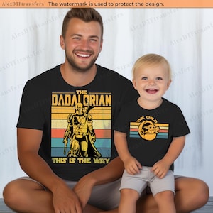 K&ouml;nnte beinhalten: Schwarze T-Shirts mit passenden Designs. Ein Shirt sagt "THE DADALORIAN THIS IS THE WAY" mit einer Mandalorianer-Grafik. Das andere Shirt sagt "THE CHILD" mit einer Grogu-Grafik. Beide Shirts haben einen Retro-Stil.