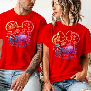 May include: Red t-shirts featuring a colorful Disney design with the text "Disney 2020". The design includes a castle, fireworks, and a Mickey Mouse ear silhouette. The shirts are short-sleeved.