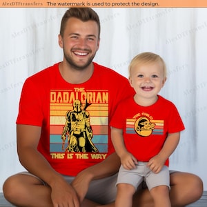 K&ouml;nnte beinhalten: Rote T-Shirts mit passenden Grafiken. Eines zeigt "THE DADALORIAN" mit einer Mandalorianer-Grafik und "THIS IS THE WAY". Das andere zeigt "THE CHILD" mit einer Grogu-Grafik.