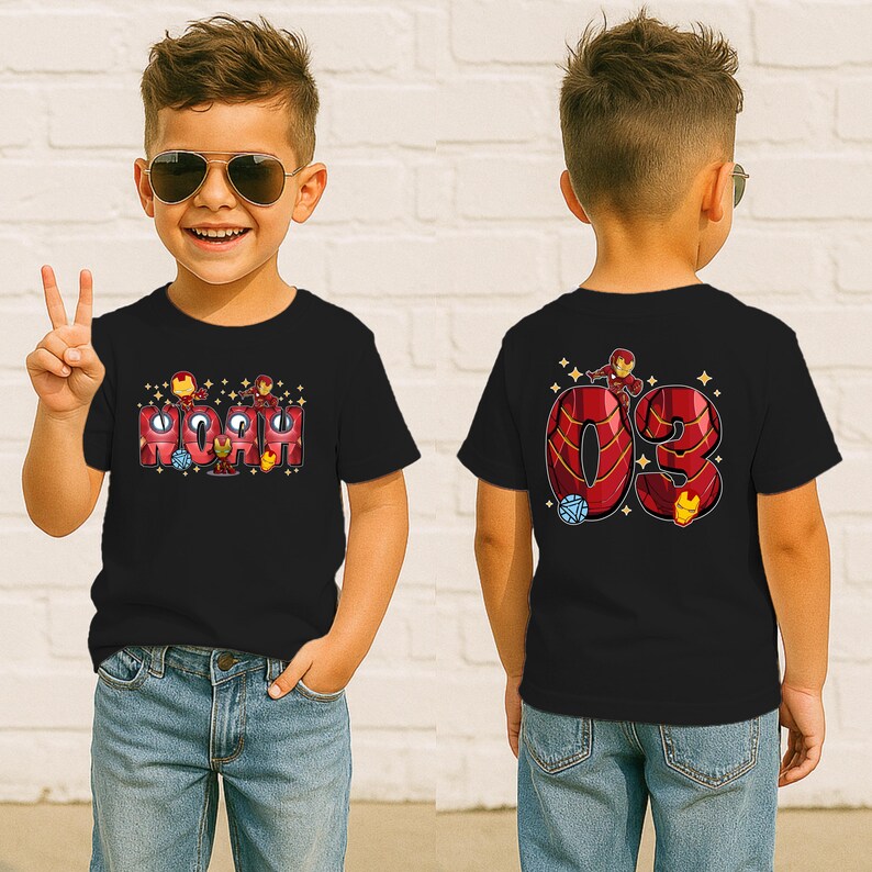 May include: Black t-shirt featuring the name "NOAH" in red and gold letters with Iron Man graphics. The back of the shirt displays the number "03" with Iron Man and other graphics. The boy is wearing blue jeans.