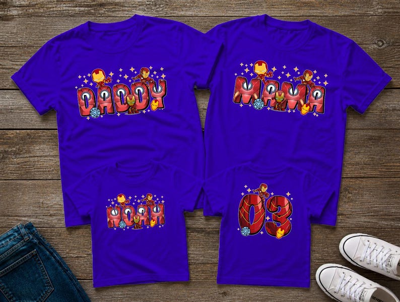 May include: Four purple t-shirts with Iron Man-themed designs. Two shirts say "Daddy" and "Mama" in red bubble letters, with Iron Man figures. The other two shirts have "Mama" and the number "03" in a similar style.