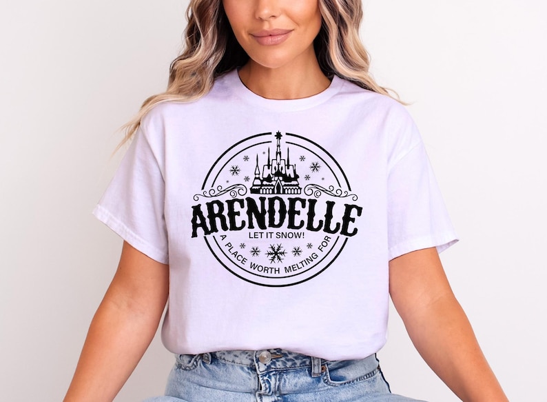 Op de afbeelding: Wit T-shirt met een zwart cirkelvormig ontwerp. Het ontwerp bevat het woord "ARENDELLE", de zin "LET IT SNOW!", een kasteelillustratie en de woorden "A PLACE WORTH MELTING FOR".