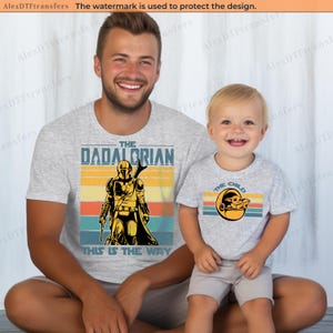 K&ouml;nnte beinhalten: Zwei passende hellgraue T-Shirts mit Star Wars-Motiven. Eines zeigt "The Dadalorian" mit einer Mandalorianer-Figur, das andere "The Child" mit Grogu. Beide Shirts haben ein Retro-Sonnenuntergangsdesign.
